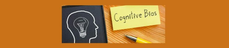 Cognitive Biases and Their Impact on Consumer Behavior (1). Medium brown background. Light wood table, left side, black chalk board with a human head outline, a sketch of a light bulb. Right side, yellow sicky note " Cognitive Bias" written in black pen. Yellow pen laying on its side with silver end,.